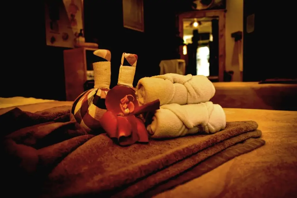 In warm verlichte massageruimte in Amersfoort bij Bonzai24 een ingezoomde massagetafel met een bruine handdoek, twee opgerolde handdoeken en twee kruidenstempels.