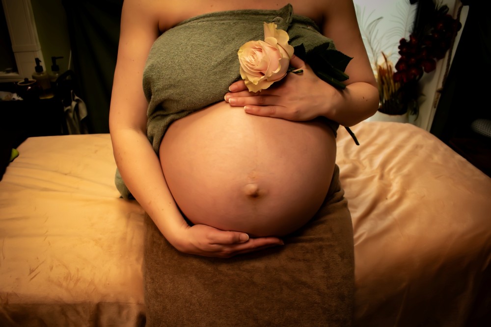 Een Zwanger vrouw zit ontspannend met een hand op haar zwangerebuik en andere hand houd ze een witte roos bloem vast afbeelding is bedoeld voor massage keuze zwangerschap massage