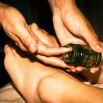 Handen van een masseur die een verzorgende balsem uit een potje aanbrengen op de voeten van een klant tijdens een ontspannende massage.