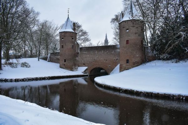 De Koppelpoort in Amersfoort centrum bedekt met sneeuw, met twee middeleeuwse torens en een brug over het water.