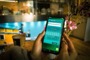 Persoon gebruikt een smartphone in een café in Amersfoort om online een datum en tijd te reserveren via een reserveringsapp, met koffie en bloemen op tafel.