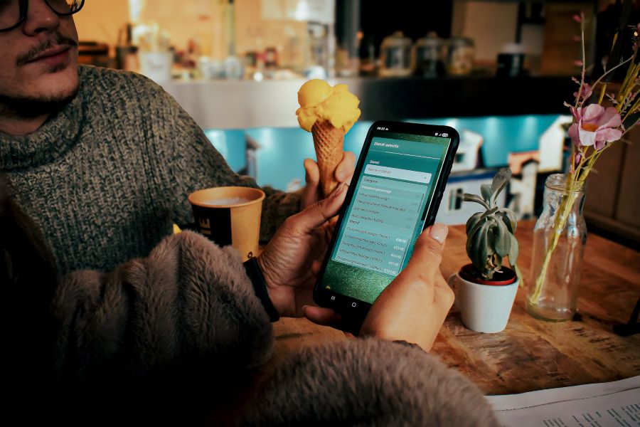 Persoon zit in een café in Amersfoort met een ijsje en koffie terwijl hij via een smartphone online een reservering bekijkt of aanpast.