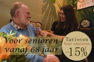 Een oudere man zit lachend in een huiskamer terwijl een jonge zorgmedewerker hem een pasje overhandigt. Op de afbeelding staat de tekst: “Voor senioren vanaf 68 jaar” en “Tarieven voor senioren –15%”.